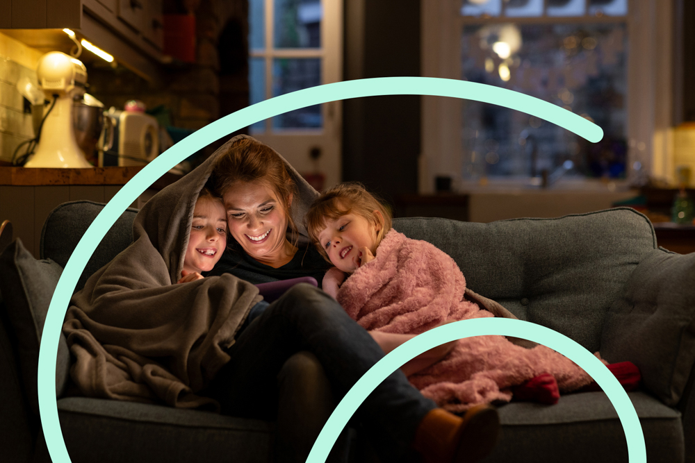 Woman sharing book on couch with two children either side under blankets